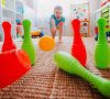 children a boy throws ball into a home bowling alley and smashes the bowling pins